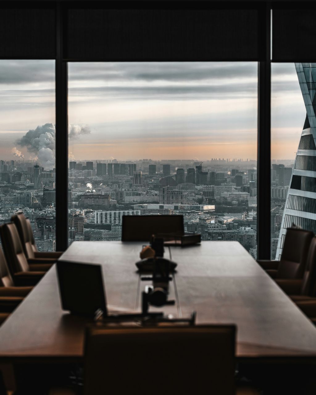 An empty boardroom with a long wooden table, looking out over a city skyline at dusk